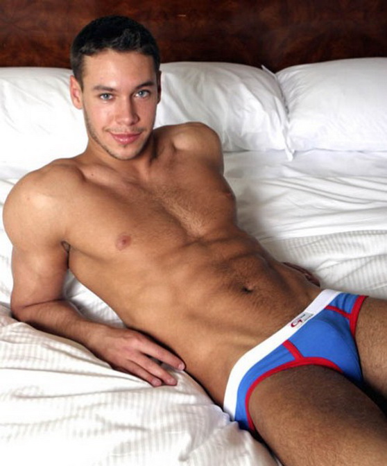 глуповатый паренек в цветных плавках позирует в кровати, фото молодых мужчин