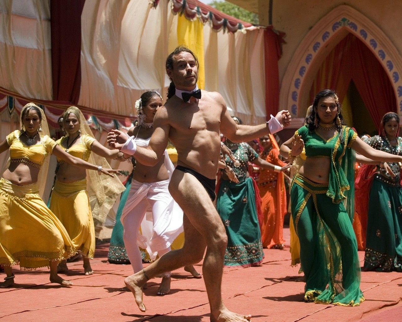 голый мужчина в галстуке-бабочке танцует с индийскими танцовщицами