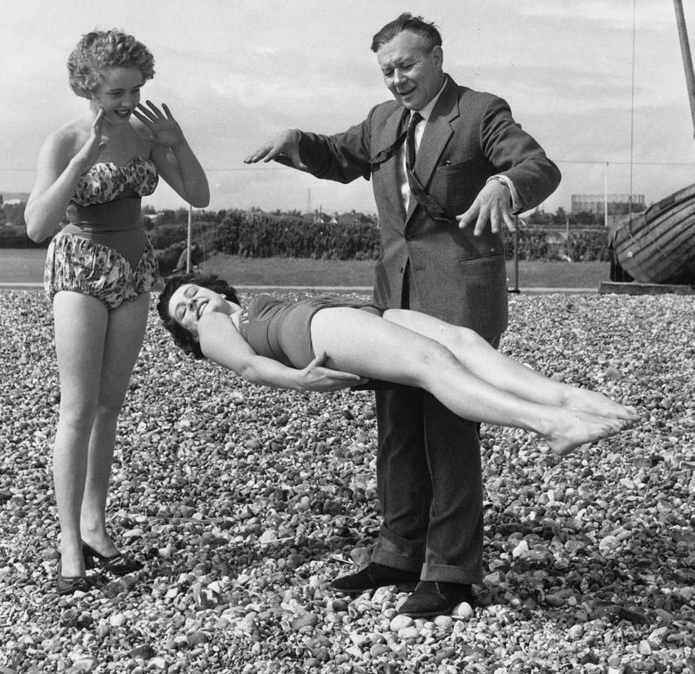 маг на пляже поднимает в воздух лежащую девушку в купальнике, ретро фото действующего мага