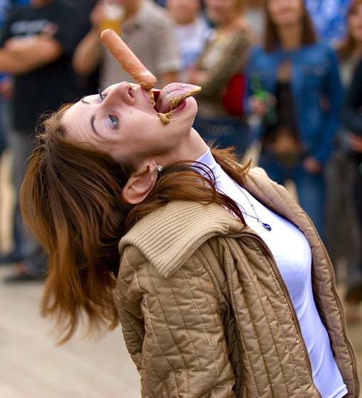 не поймала! девушка ловит ртом сосиску с горчицей. веселая картинка для взрослых
