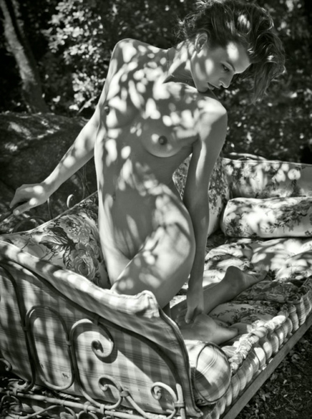 Мила Йовович в голом виде стоит на коленях на садовом диване