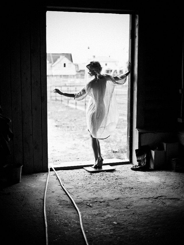 черно-белое фото Полины Гагариной стоящей голышом в прозрачной накидке в распахнутых дверях сеновала